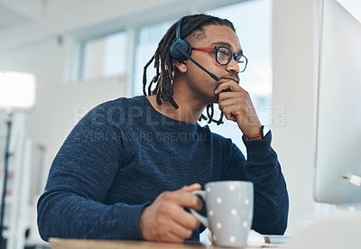 Buy stock photo Shot of a young businessman wearing a headset while working on a computer in an office