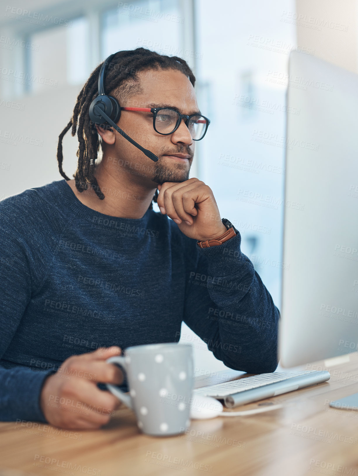 Buy stock photo Shot of a young businessman wearing a headset while working on a computer in an office