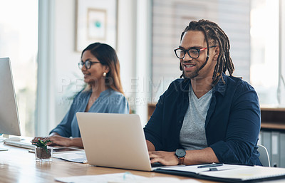 Buy stock photo Shot of a young businessman working on a laptop in an office with his colleague in the background
