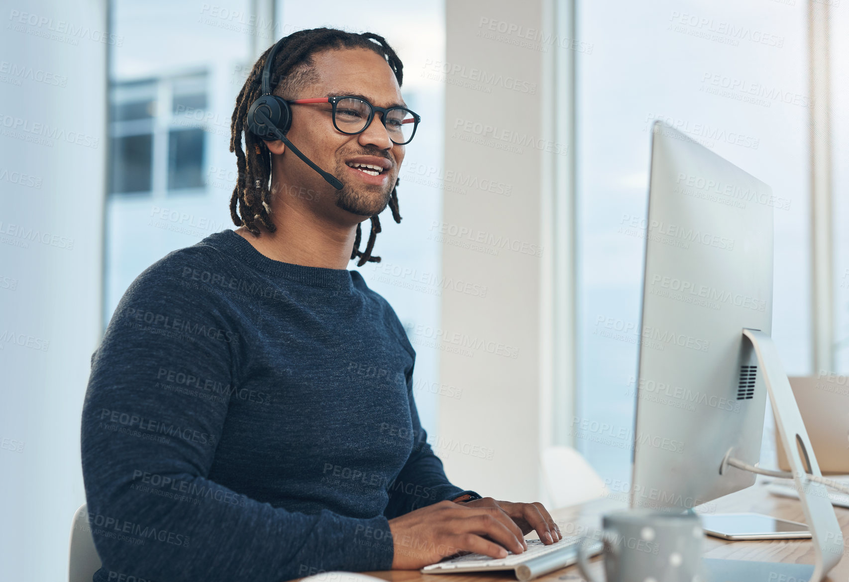 Buy stock photo Shot of a young businessman wearing a headset while working on a computer in an office