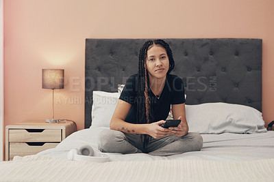 Buy stock photo Portrait of a young woman using a smartphone while relaxing on her bed at home