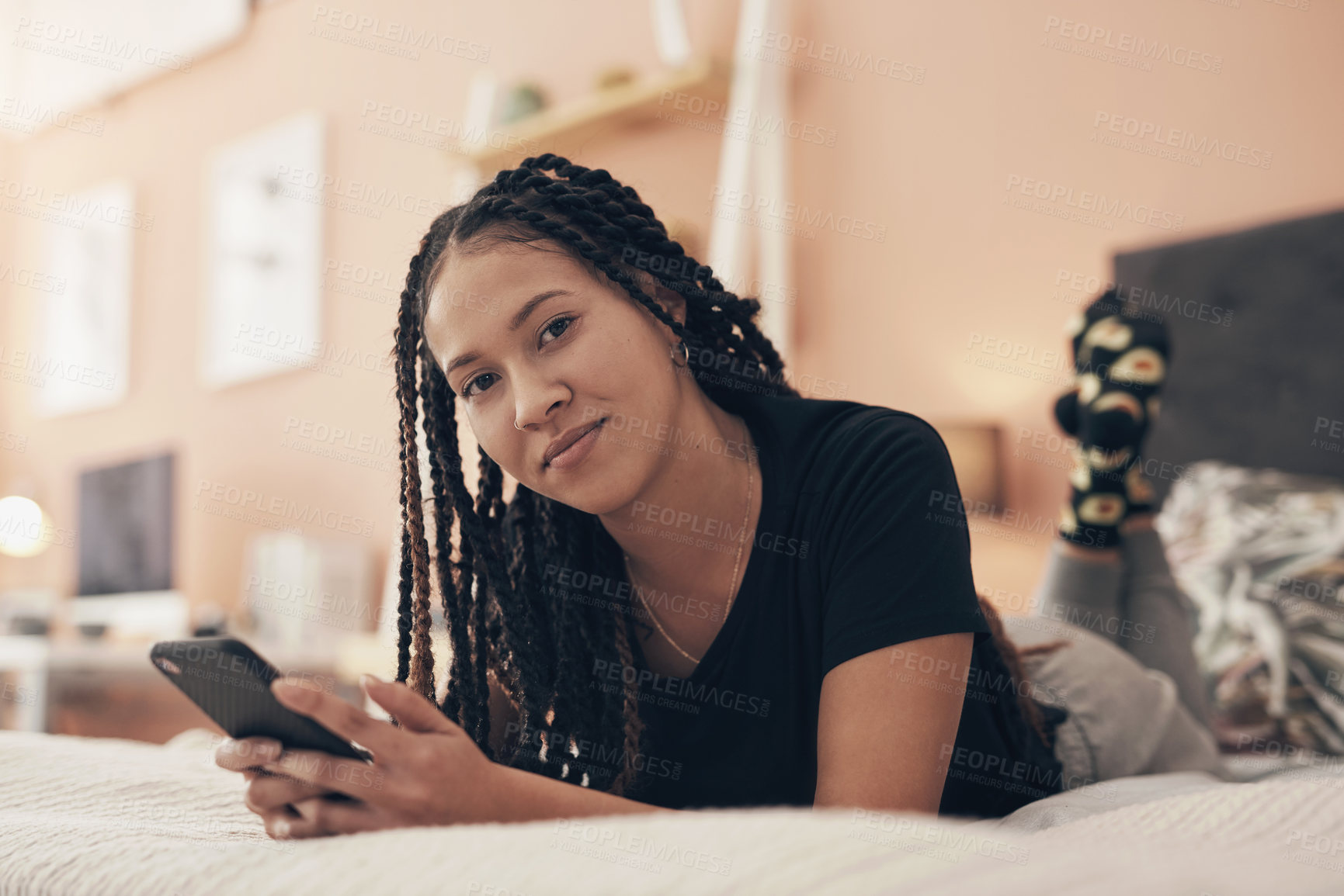 Buy stock photo Portrait of a young woman using a smartphone while relaxing on her bed at home