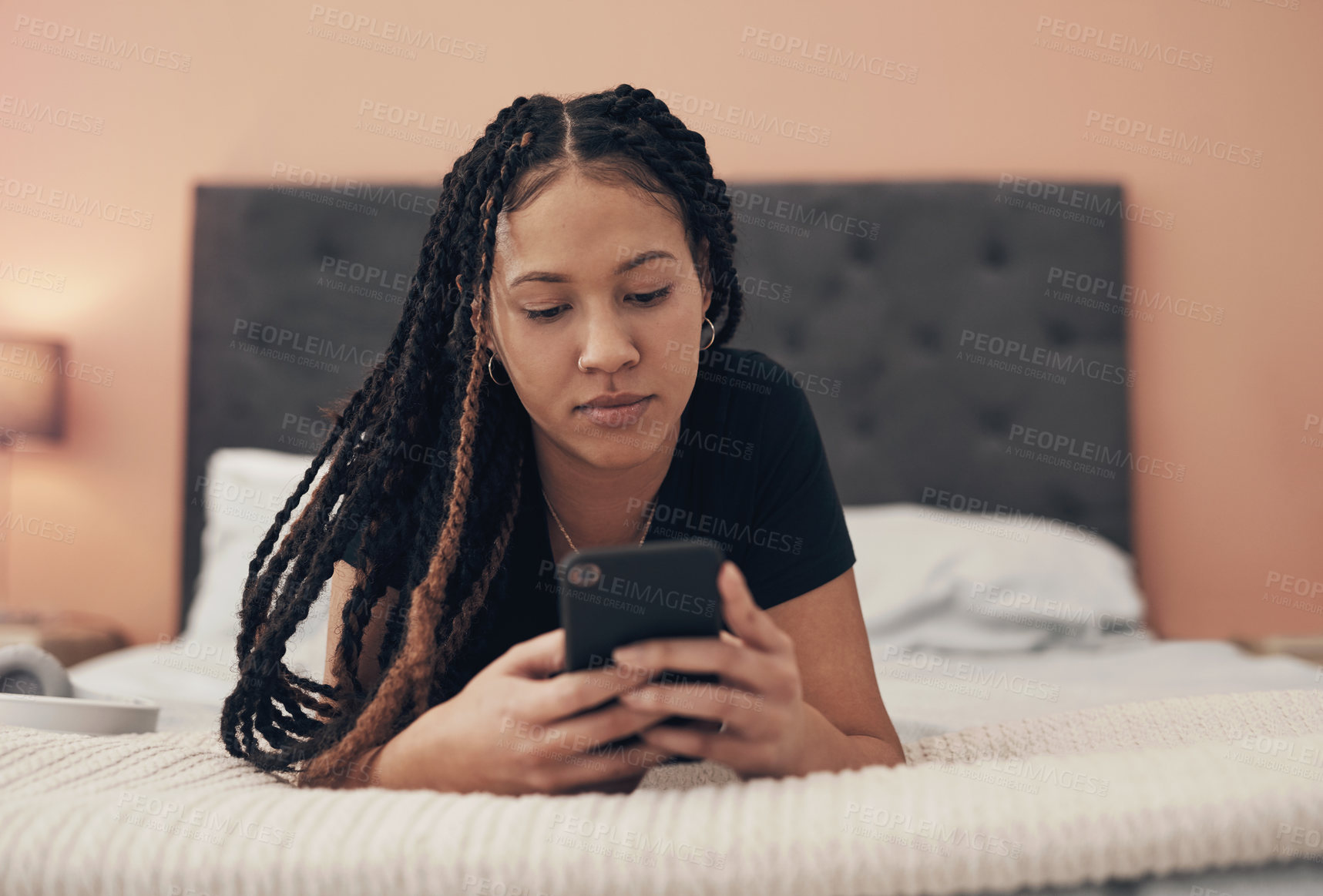 Buy stock photo Shot of a young woman using a smartphone while relaxing on her bed at home