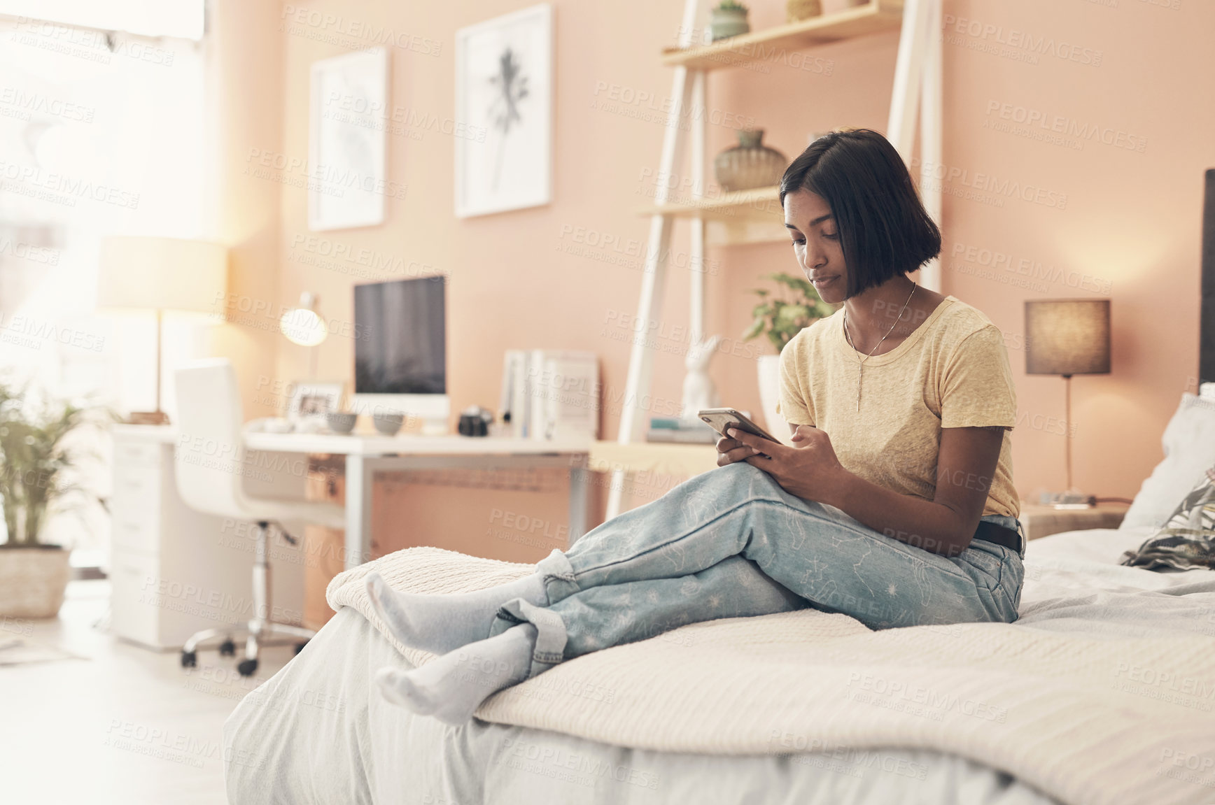 Buy stock photo Shot of a young woman using a smartphone while relaxing on her bed at home