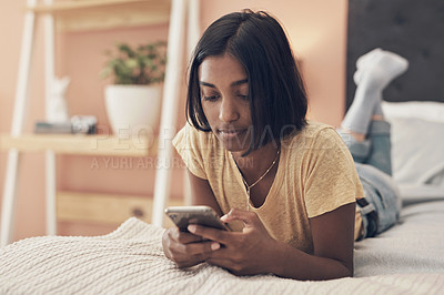 Buy stock photo Shot of a young woman using a smartphone while relaxing on her bed at home