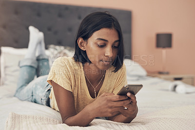 Buy stock photo Shot of a young woman using a smartphone while relaxing on her bed at home