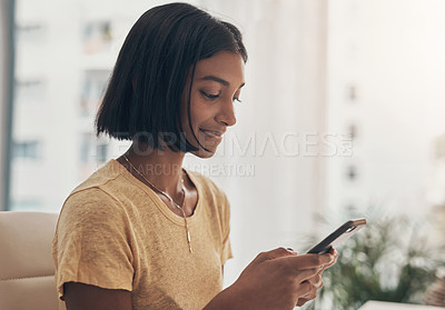 Buy stock photo Shot of a young woman using a smartphone while working from home