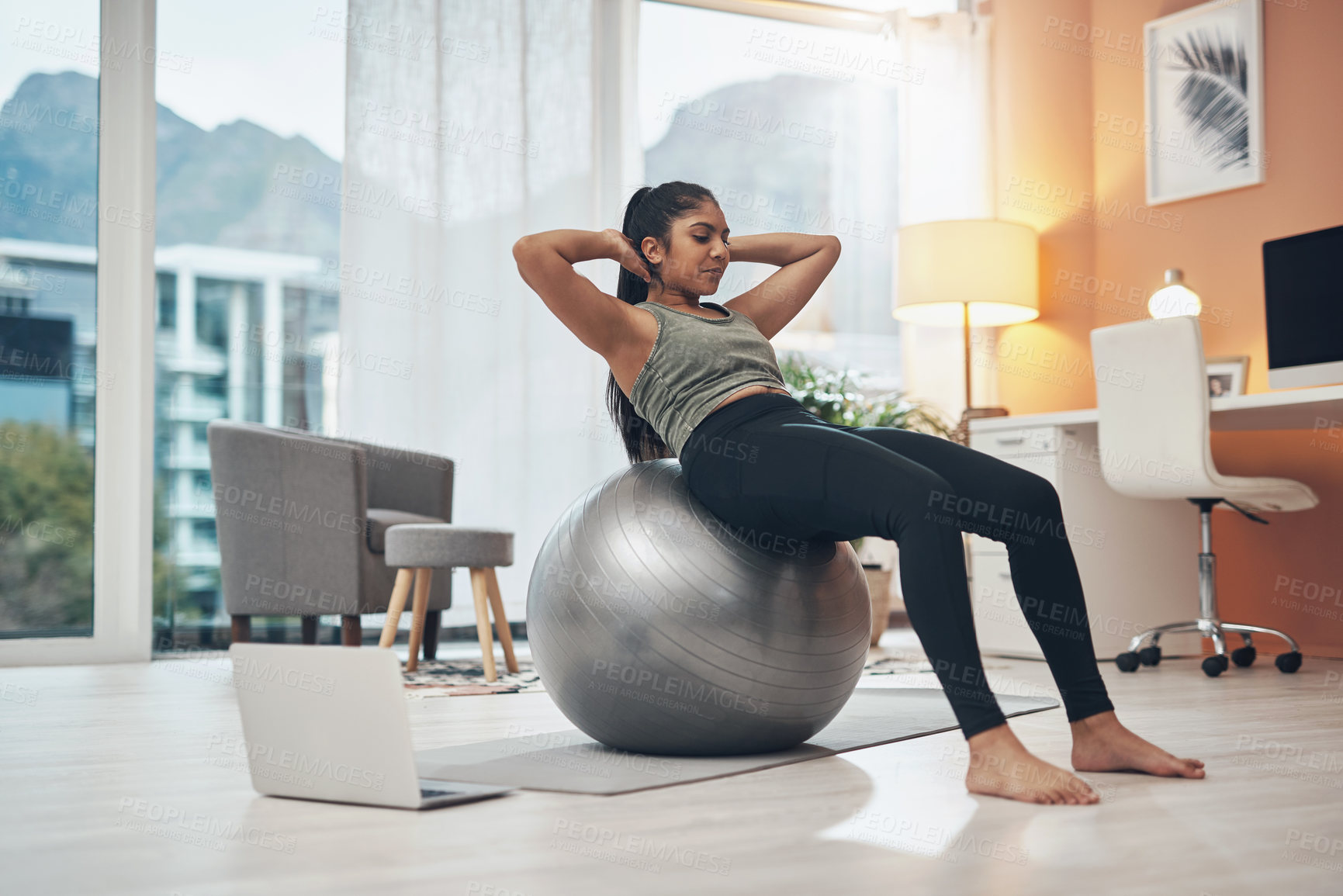 Buy stock photo Shot of a woman working out in her living room with her laptop next to her