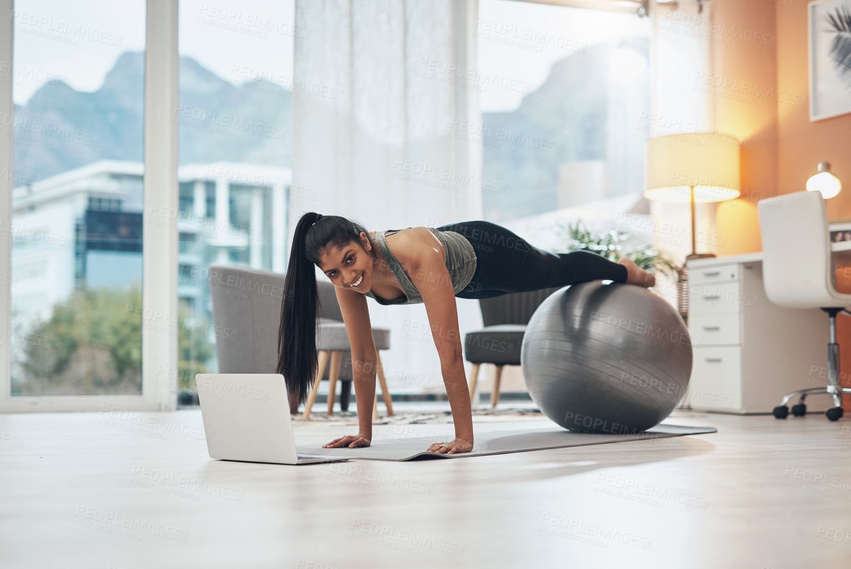 Buy stock photo Shot of a woman working out in her living room with her laptop in front of her