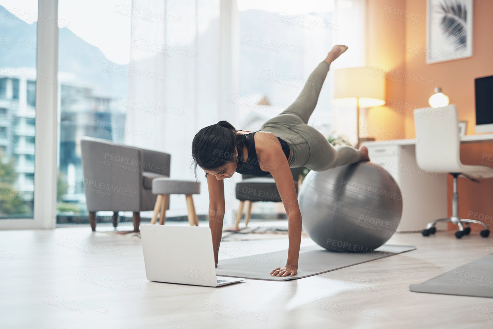Buy stock photo Shot of a woman working out in her living room with her laptop in front of her