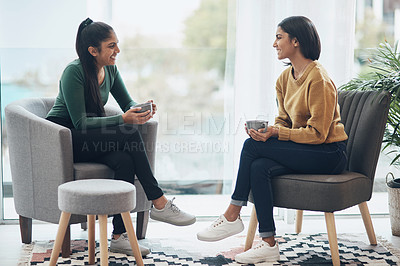 Buy stock photo Shot of two young women drinking coffee while sitting together at home