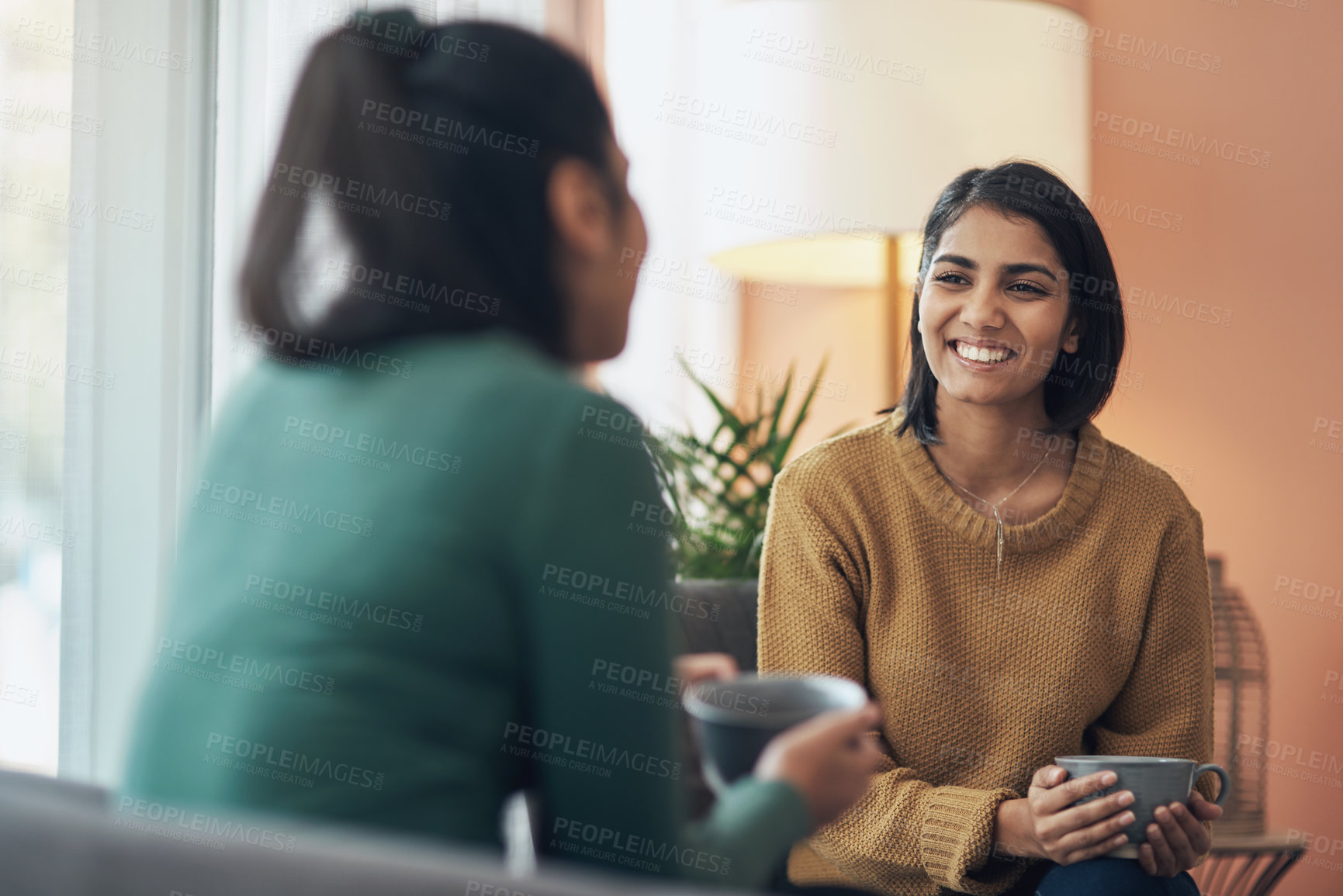 Buy stock photo Shot of two young women drinking coffee while sitting together at home