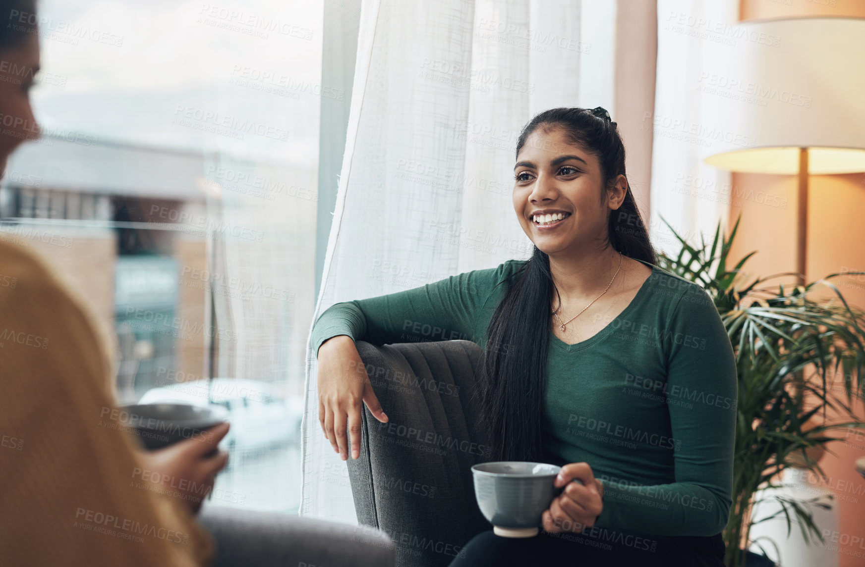 Buy stock photo Shot of two young women drinking coffee while sitting together at home