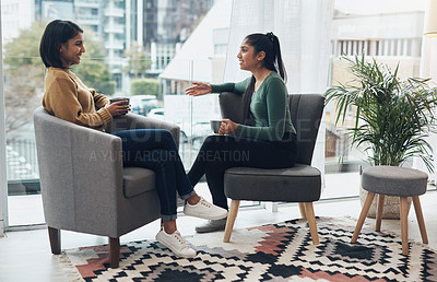 Buy stock photo Shot of two young women drinking coffee while sitting together at home