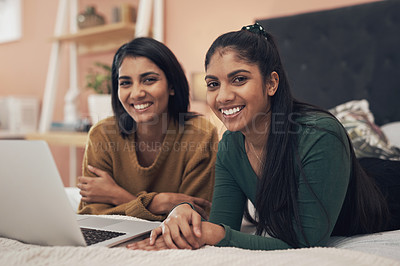 Buy stock photo Shot of two young women using a laptop while lying together on a bed