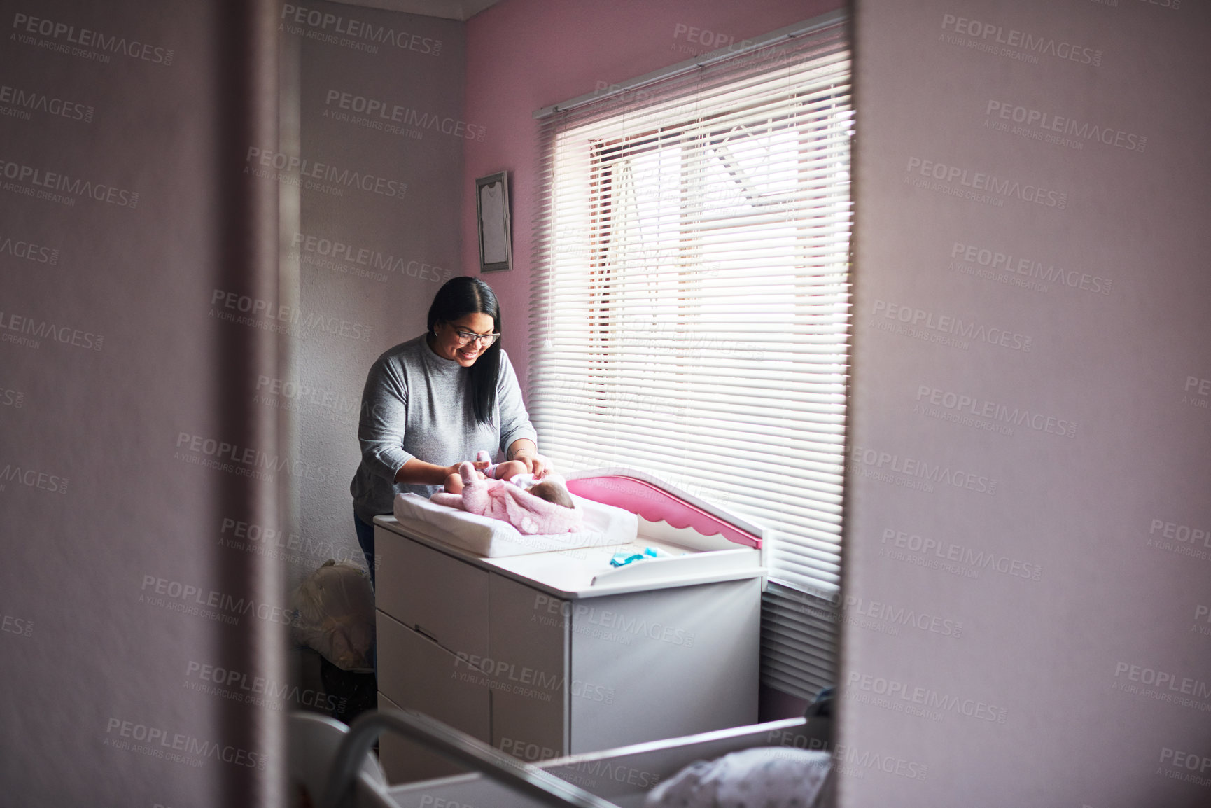 Buy stock photo Shot of a young woman changing her baby girl’s clothing at home
