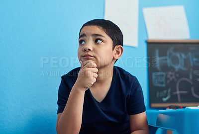 Buy stock photo Shot of an adorable little boy looking thoughtful while completing a school assignment at his desk