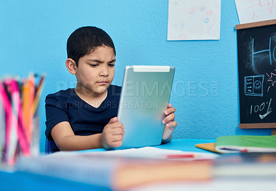 Buy stock photo Shot of an adorable little boy using a digital tablet to complete a school assignment at his desk