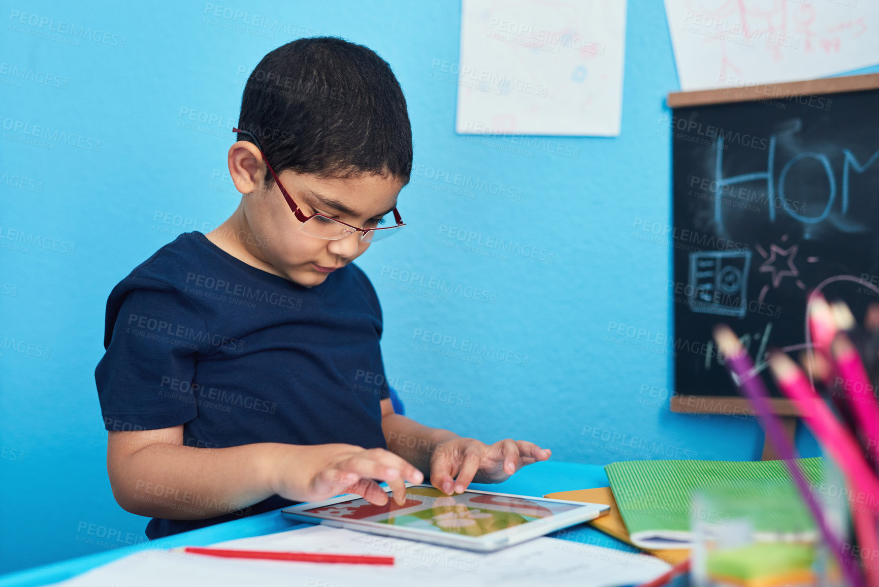 Buy stock photo Shot of an adorable little boy using a digital tablet to complete a school assignment at his desk