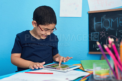 Buy stock photo Shot of an adorable little boy using a digital tablet to complete a school assignment at his desk