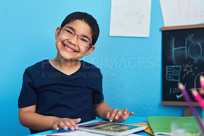 Buy stock photo Portrait of an adorable little boy using a digital tablet to complete a school assignment at his desk