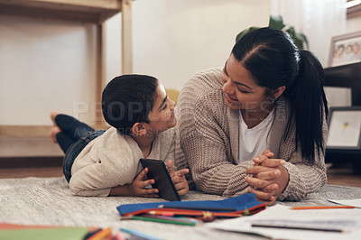 Buy stock photo Shot of an adorable little boy using a smartphone while completing a school assignment with his mother at home