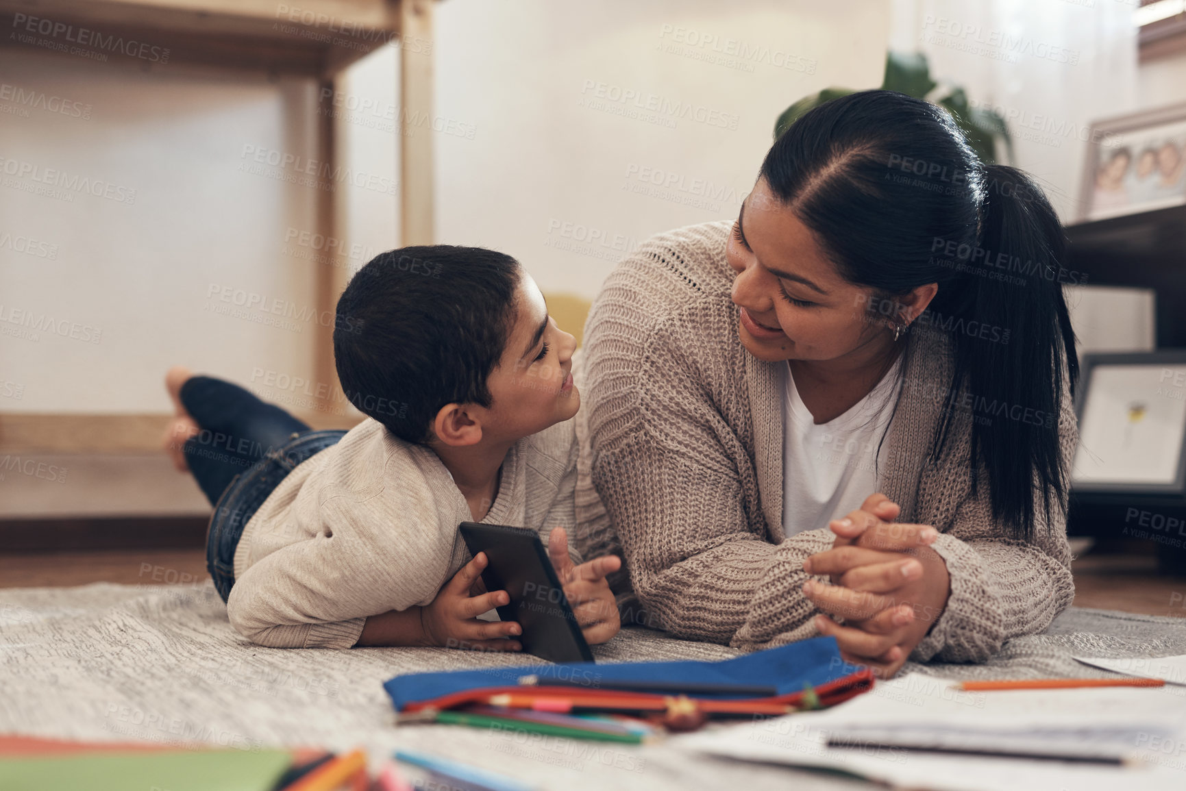 Buy stock photo Shot of an adorable little boy using a smartphone while completing a school assignment with his mother at home