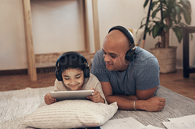 Buy stock photo Shot of an adorable little boy using a digital tablet and headphones with his father at home