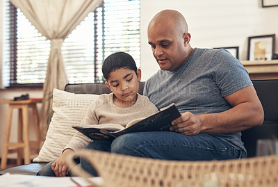 Buy stock photo Shot of an adorable little boy reading a book with his father on the sofa at home