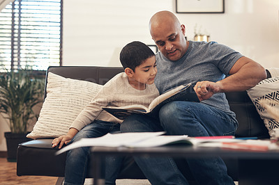 Buy stock photo Shot of an adorable little boy reading a book with his father on the sofa at home