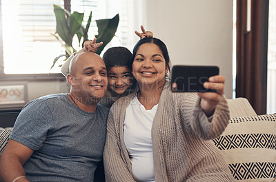 Buy stock photo Shot of a happy young family taking selfies with a smartphone on the sofa at home