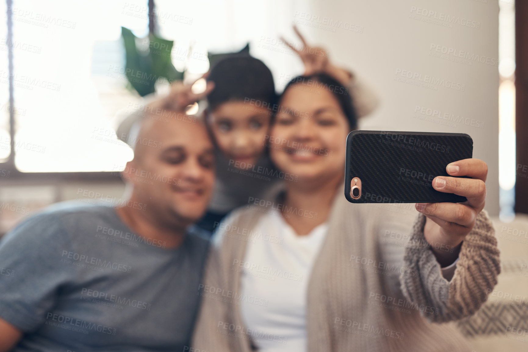 Buy stock photo Shot of a happy young family taking selfies with a smartphone on the sofa at home