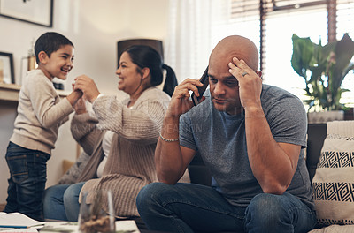 Buy stock photo Shot of a man using a smartphone and looking stressed while his wife and son play together in the background