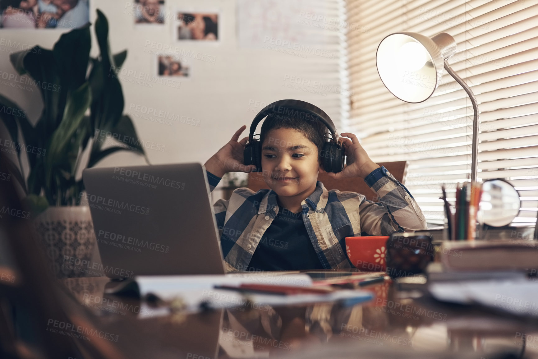 Buy stock photo Shot of an adorable little boy using a laptop and headphones while completing a school assignment at home