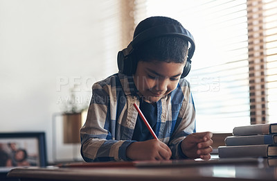 Buy stock photo Shot of an adorable little boy using a digital tablet and headphones while completing a school assignment at home