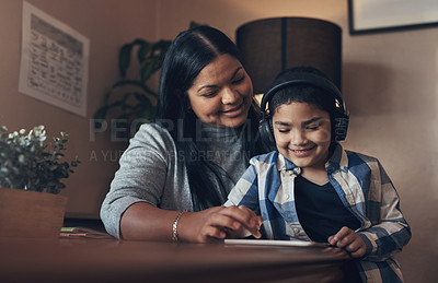 Buy stock photo Shot of an adorable little boy using a digital tablet and headphones while completing a school assignment with his mother at home