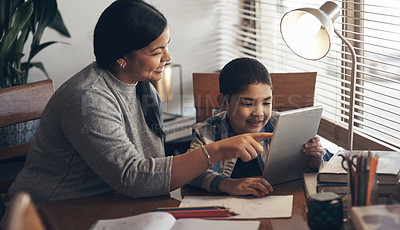 Buy stock photo Shot of an adorable little boy using a digital tablet while completing a school assignment with his mother at home