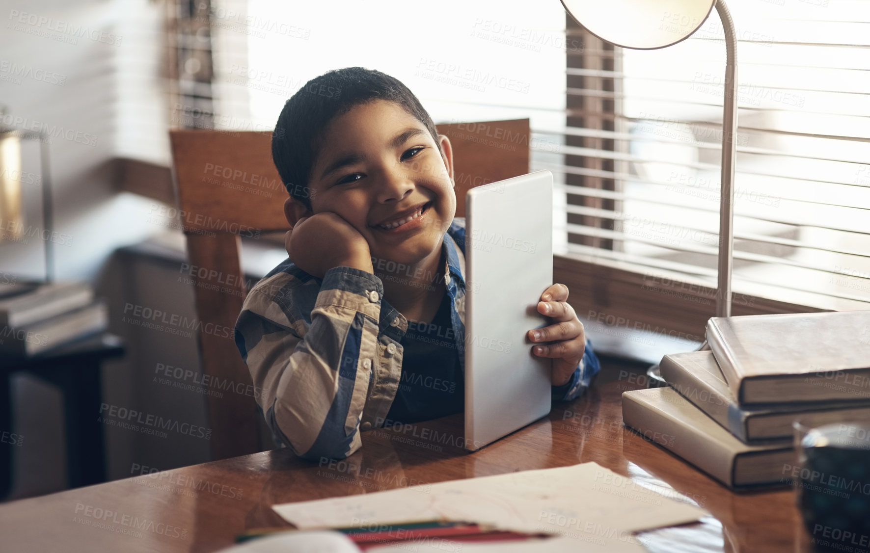 Buy stock photo Shot of an adorable little boy using a digital tablet while completing a school assignment at home