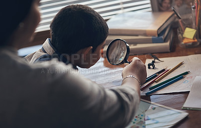 Buy stock photo Shot of an adorable little boy using a magnifying glass while completing a school assignment with his mother at home