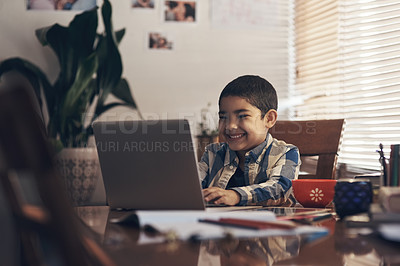Buy stock photo Shot of an adorable little boy using a laptop while completing a school assignment at home