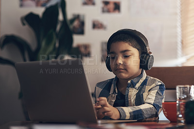 Buy stock photo Shot of an adorable little boy using a laptop and headphones while completing a school assignment at home