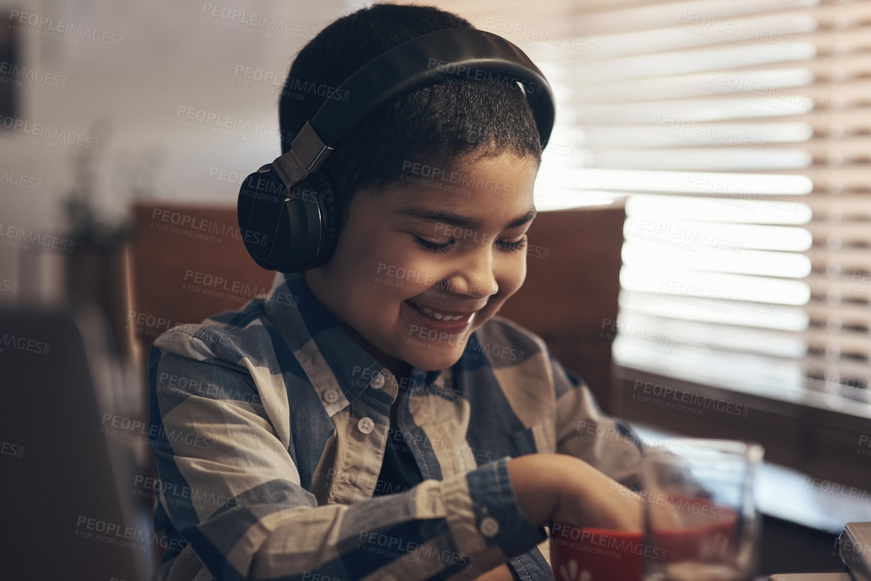 Buy stock photo Shot of an adorable little boy using a laptop and headphones while completing a school assignment at home