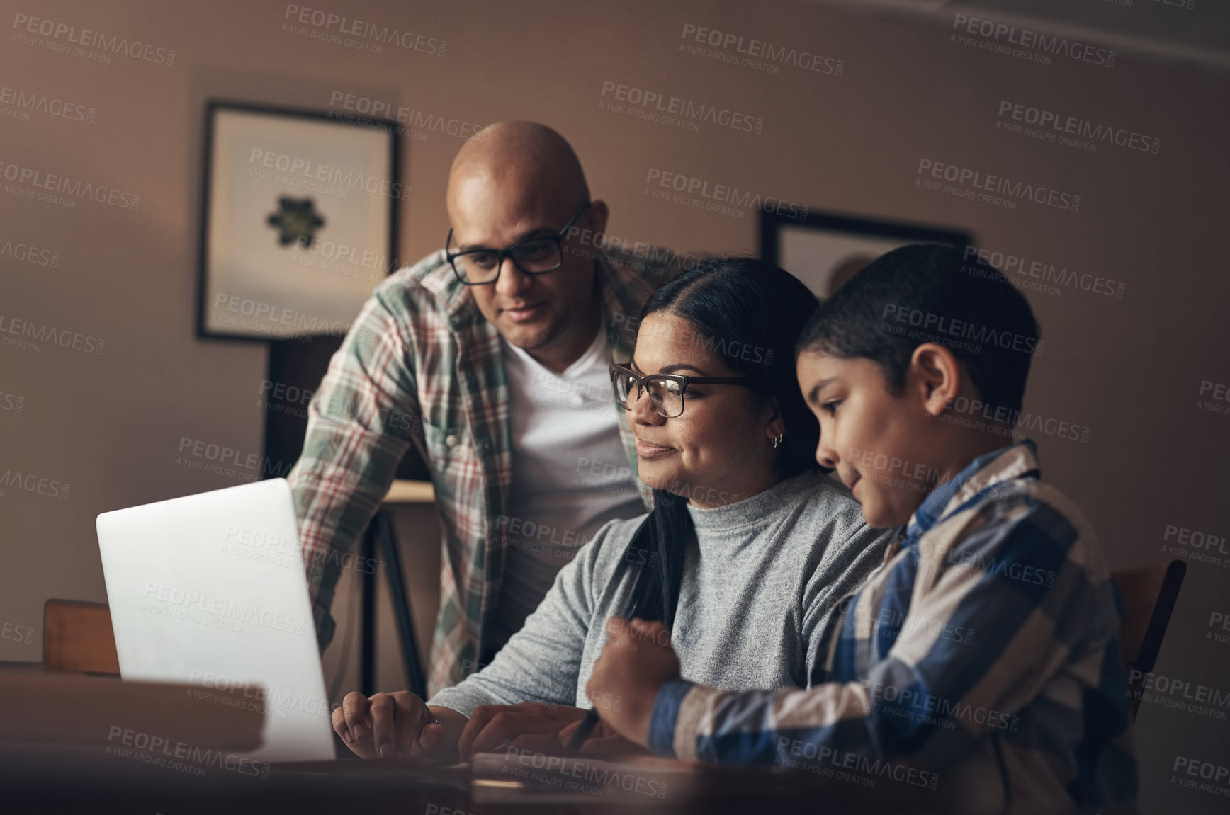 Buy stock photo Shot of an adorable little boy using a laptop while completing a school assignment with his parents at home