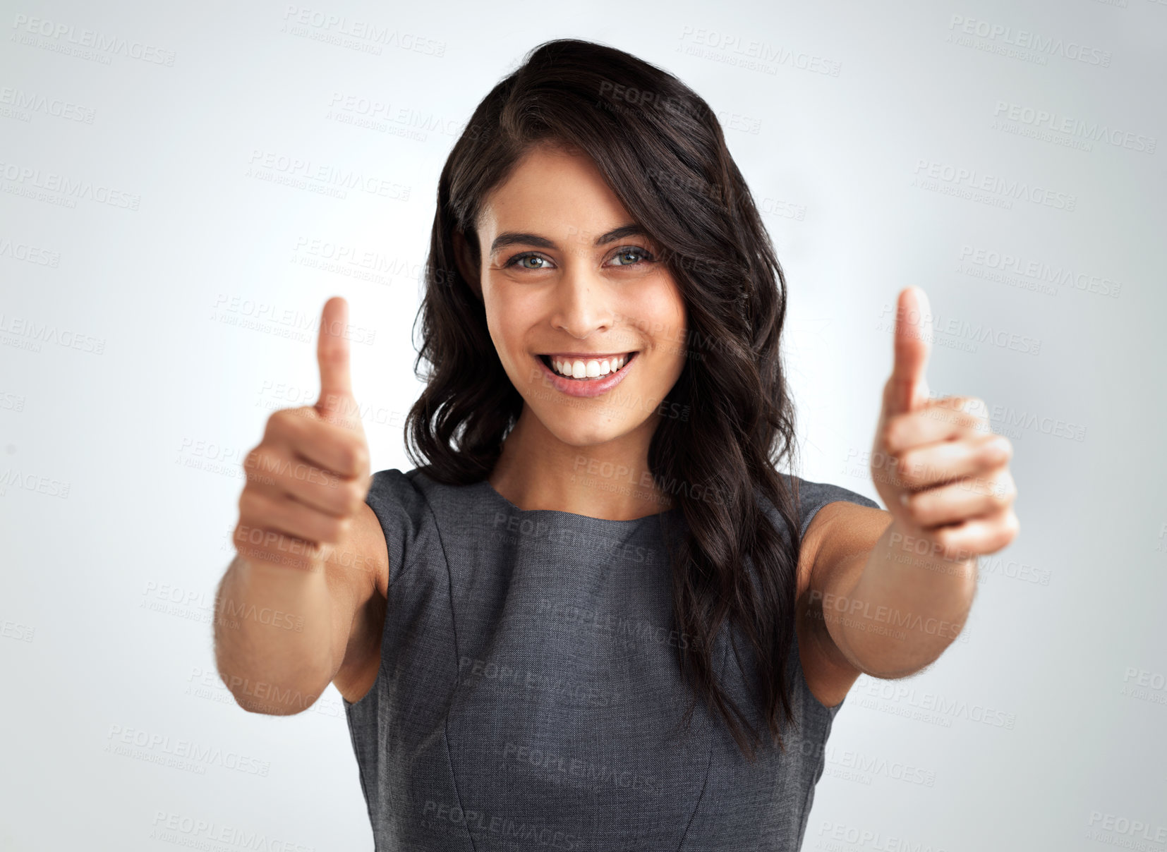 Buy stock photo Shot of a young woman showing thumbs up while standing against a grey background