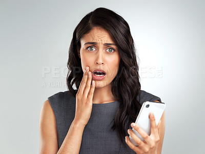 Buy stock photo Shot of a young woman using her cellphone while standing against a grey background