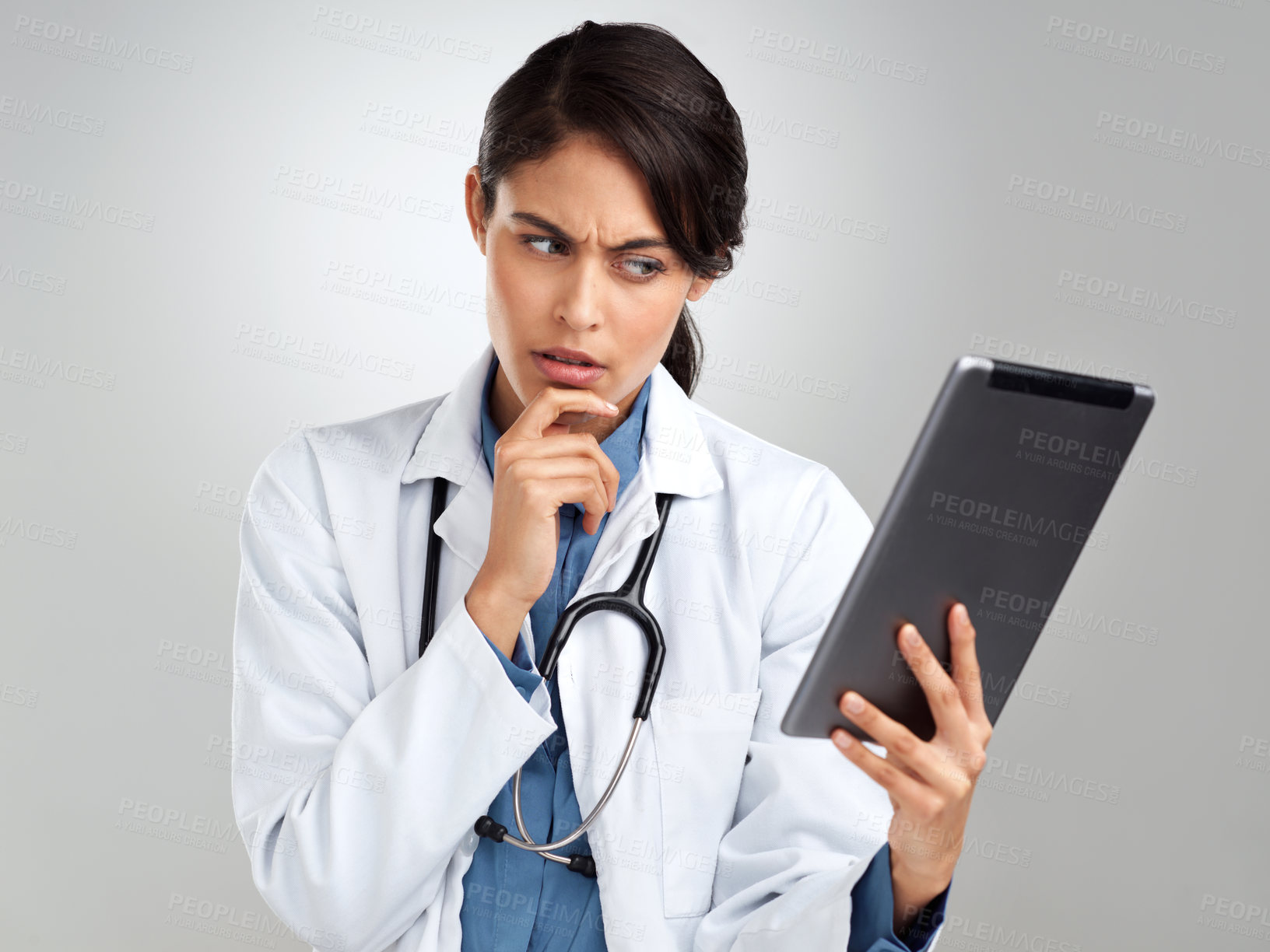 Buy stock photo Studio shot of a young doctor using a digital tablet and looking unsure a grey background