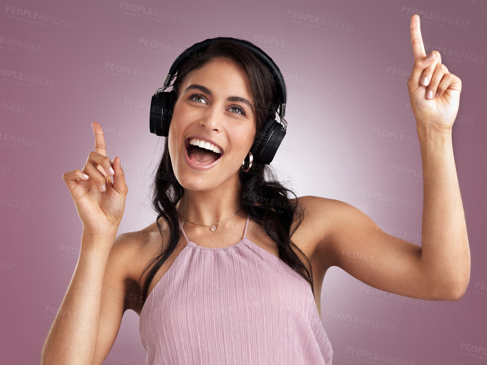 Buy stock photo Shot of a beautiful young woman pointing up while listening to music wearing headphone against a pink background