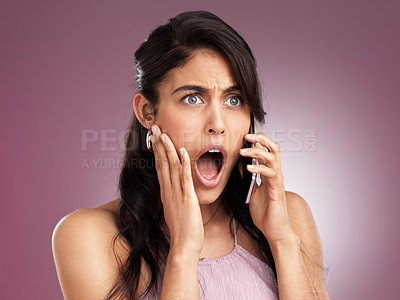 Buy stock photo Shot of a beautiful young woman looking shocked with her hand against her cheek while talking on a mobile phone against a pink background