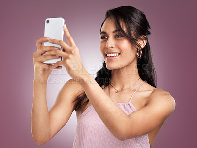Buy stock photo Shot of a beautiful young woman holding up her mobile phone to take a selfie against a pink background