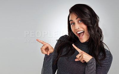 Buy stock photo Shot of a beautiful young woman pointing at copy space against a grey background